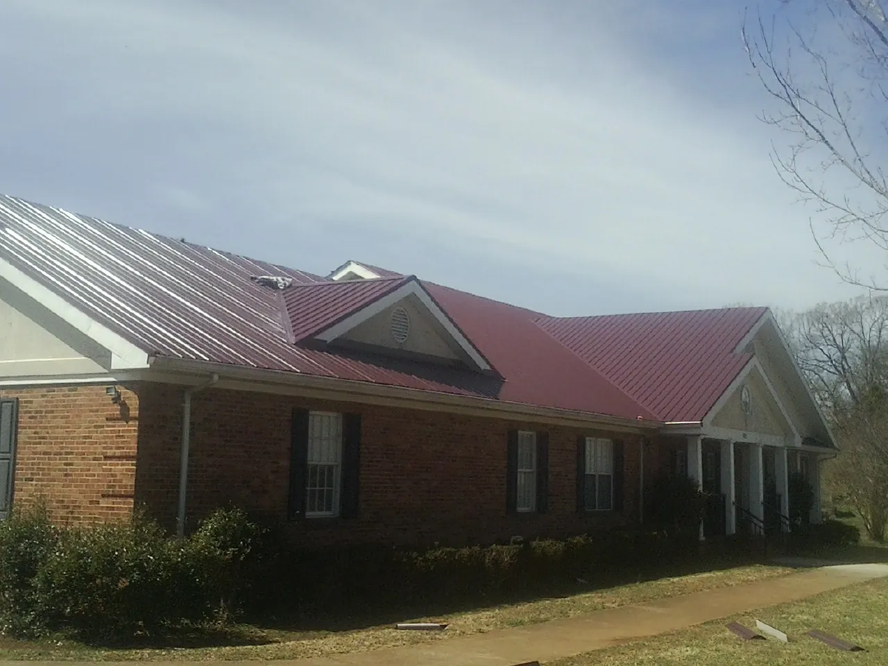 Red metal roof with gabled entries on a long brick building, from a Hail Damage Roof Repair job in Woodstown