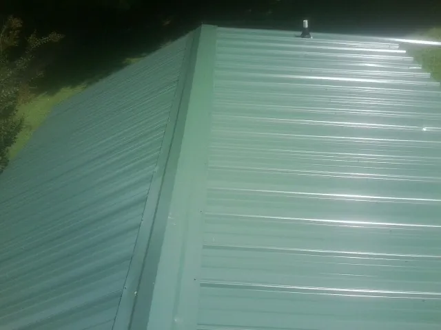 New green metal panels meeting at the ridge of a roof — Flat Roof Repair work by our crew in Woodstown