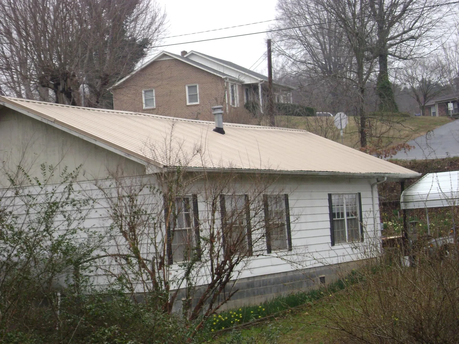 Tan metal roof on a white sided house set into a hillside — Commercial Roofing by Roofing Brothers in Woodstown